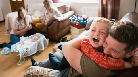 Smiling family with baby in lounge - Totally Life